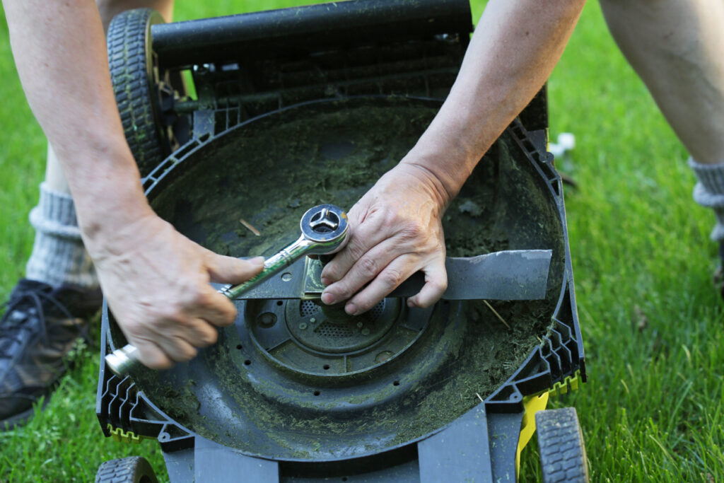 A man uses a work tool to fasten a nut on a battery-powered lawn mower outdoors.